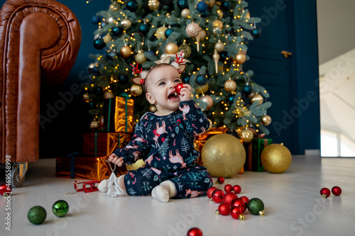 baby in pajamas plays with Christmas decorations near the Christmas tree