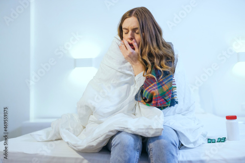 woman with fever, measuring body temperature with a thermometer, blowing her nose in bed, coughing.