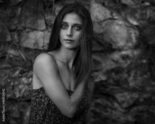 Black and white image of a young woman in flower print dress, exploring a woodland garden.