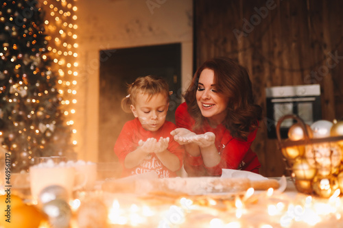 Happy mom and little daughter child in red pajamas cook Christmas ginger cookies together in the decorated kitchen during the New Year holidays at cozy home. Selective focus