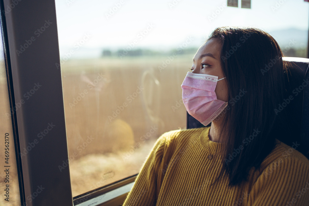 Close up of young Asian pretty woman travelling in bus with pink mask looking through the window