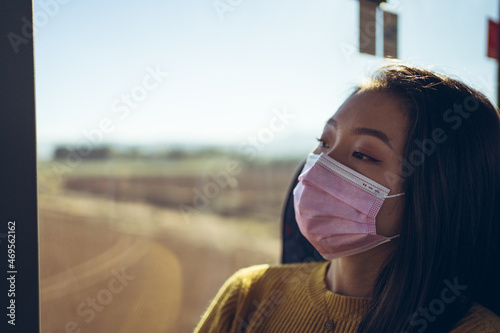 Close up of young Asian pretty woman travelling in bus with pink mask looking through the window