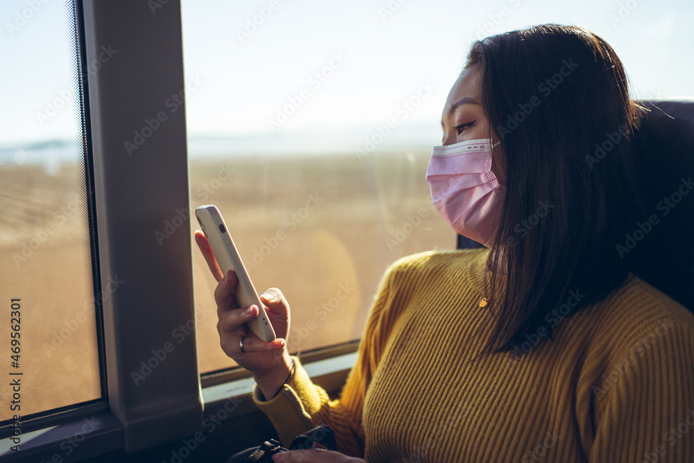 Young Asian pretty woman travelling in bus with pink mask using smartphone