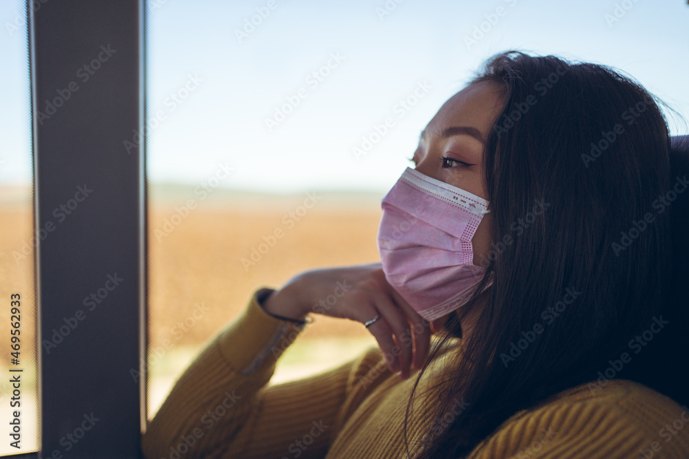 Young Asian pretty woman travelling in empty bus with pink mask looking through the window
