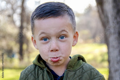 Canvas Print Funny humorous playful pouting pouty lips of young boy child outside with deep blue eyes and a green jacket