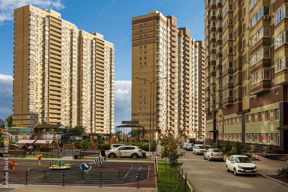 Three tall apartment buildings next to a playground and a blue sky. A new residential area of a developing city. Yellow multistory with balconies.