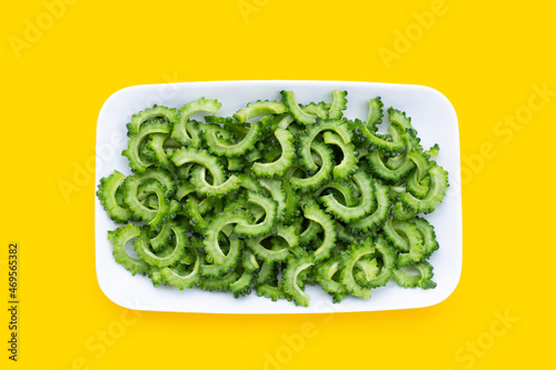 Sliced bitter gourd in white plate on yellow background.
