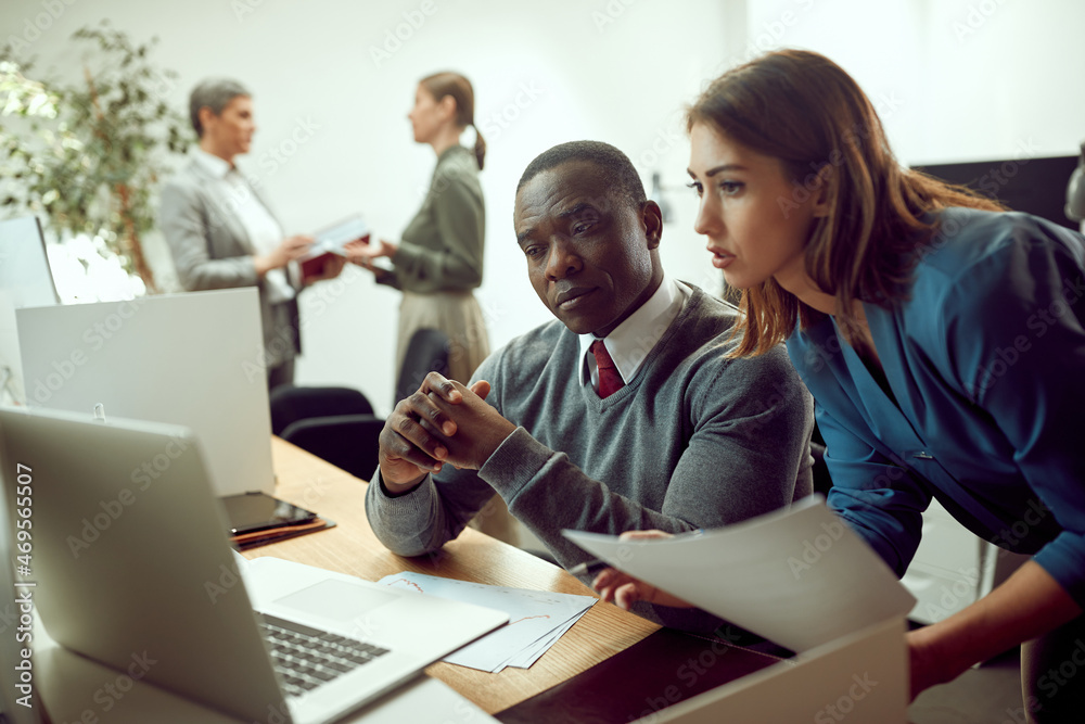 Obraz premium African American businessman and his female colleague use laptop while working on reports in office.
