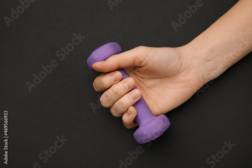 Female hand with dumbbell on dark background