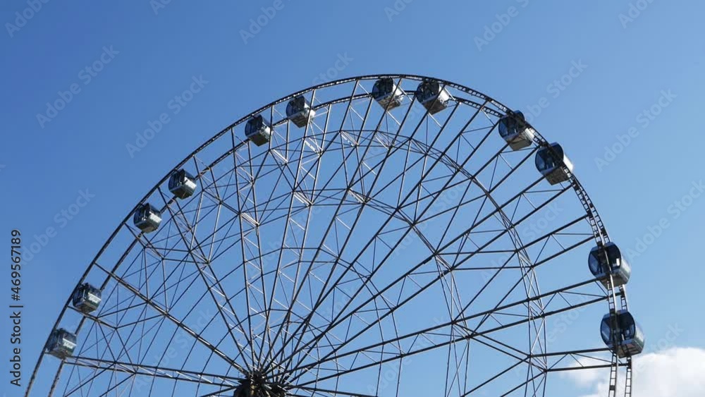 The Ferris wheel slowly rotates in the amusement park against the background of the sky. The carousel ride is fun and fun. Endless cycle. The Ferris wheel slowly rotates in the amusement park against the background of the sky. The carousel ride is fun and fun. Endless cycle.