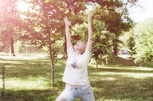 A mature woman in a T-shirt and shorts does fitness exercises and does yoga outdoors.