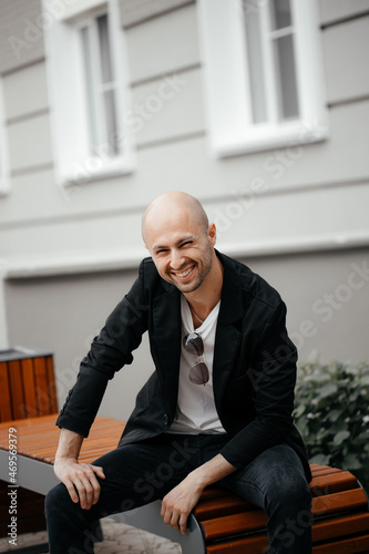 Portrait of a handsome smiling hipster man. A man dressed in a white T-shirt and jacket. A fashionable man sitting on a bench
