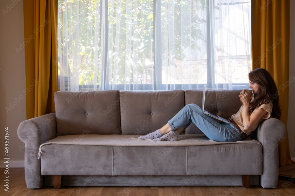 Minimalism interior. A young woman is drinking coffee during working from home.