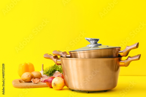 Fresh vegetables and cooking pots on color background