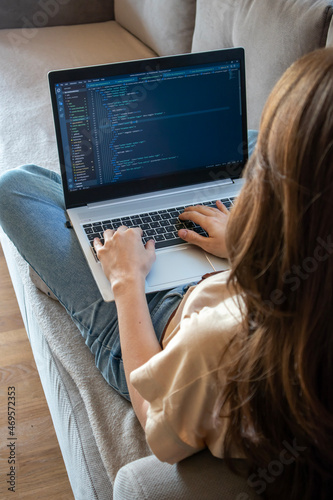 Woman working on a laptop while sitting on the sofa. A girl programmer is coding