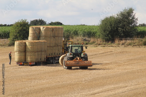 A tractor loading round hay bales on to truck for harvesting in afield Near wakefield West Yorkshire in the UK on a summers day photo