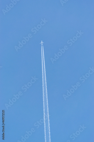 A white jet plane flies high in the blue sky and leaves behind a white trail (contrail)
