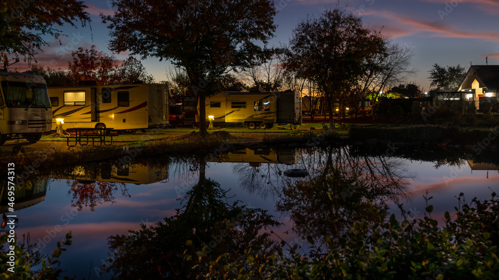Reflection in the pond of the campers parked next to it in the very early morning sunrise with a colorful sky above