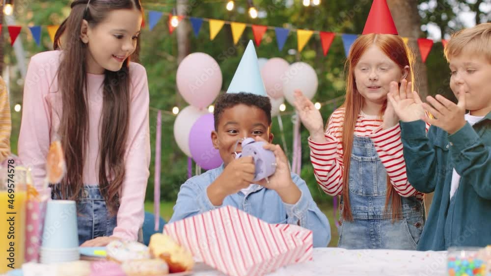 Portrait of multiracial child boy opening present and taking clock at the table with his friends. Surprise present, birthday gift, happy kids, childhood concept Portrait of multiracial child boy opening present and taking clock at the table with his friends. Surprise present, birthday gift, happy kids, childhood concept