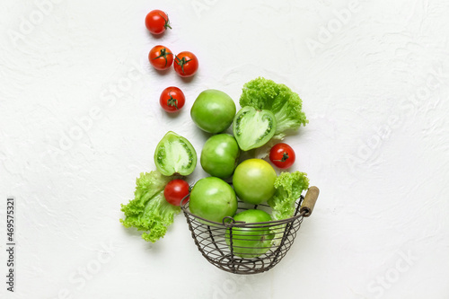 Basket with different fresh tomatoes and lettuce on white background