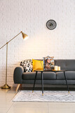 Glowing floor lamp and comfortable sofa near white brick wall