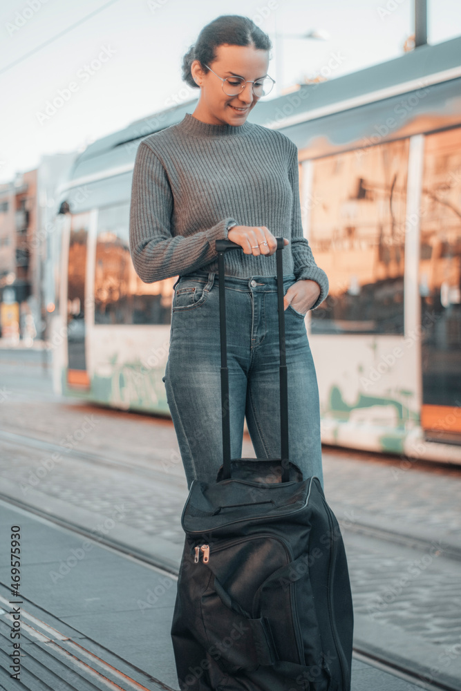 Chica entusiasmada joven de negocios esperando en la estación del metro junto con su maleta para viajar hasta la ciudad y empezar su trabajo 