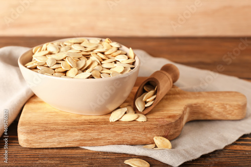 Bowl with natural pumpkin seeds on wooden background