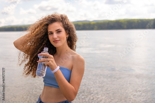 Young beautiful curly woman drinking water and posing outside