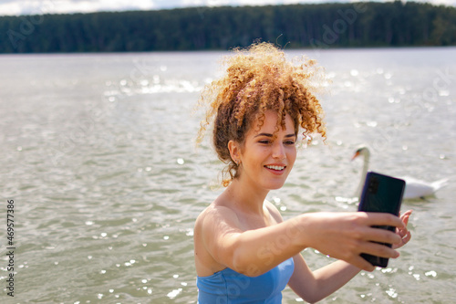 Young curly woman taking a selfie with a smartphone while outside in the nature
