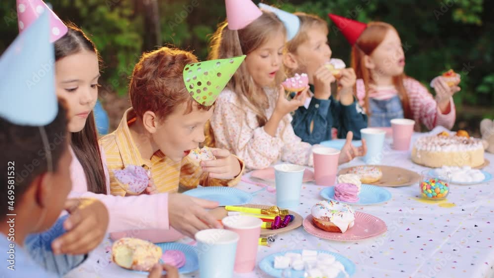 Happy birthday party. Children in party caps celebrating birthday at the nature. Kids with delicious food and gifts sitting at the table and eating. Happy children at birthday party concept Happy birthday party. Children in party caps celebrating birthday at the nature. Kids with delicious food and gifts sitting at the table and eating. Happy children at birthday party concept