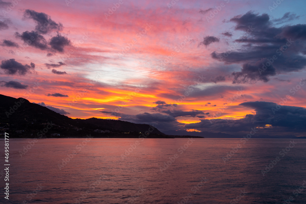Cefalù Sunset Brilliance. The sun dips below the horizon in Cefalù, painting the sky with vibrant hues of orange and pink, reflecting its brilliance over the calm waters.
