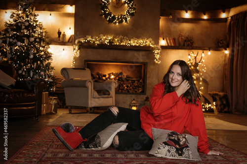 A young beautiful girl in a red sweater poses against the background of a New Year's interior.