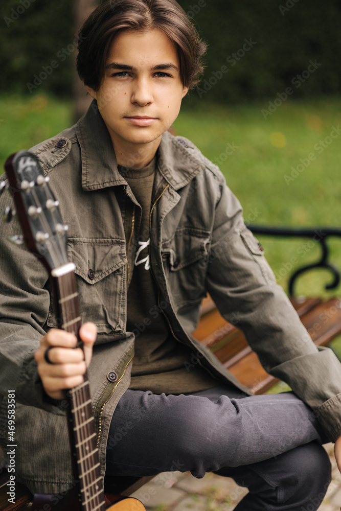 Fototapeta premium Portrait of handsome teenage boy playing guitar outdoor. Boy using classic guitar. Male alone making music