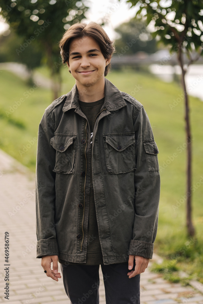 Happy teenage boy walking outdoor in the park in autumn time. Boy in khaki jacket Happy teenage boy walking outdoor in the park in autumn time. Boy in khaki jacket