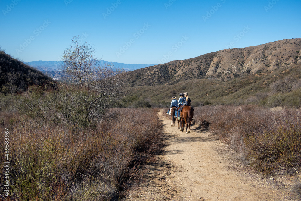 Obraz premium Equestrians Riding their Horses in the California Chaparral Hills on Beautiful Saddle Horses Along a Grassy Dry Trail