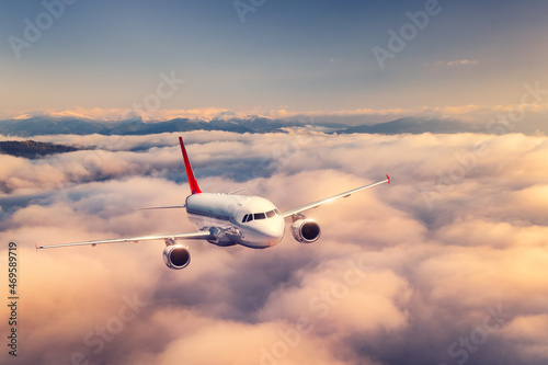 Airplane is flying above the clouds at sunset in summer. Landscape with passenger airplane, beautiful clouds, mountains, sky. Aircraft is taking off. Business travel. Commercial plane. Transport