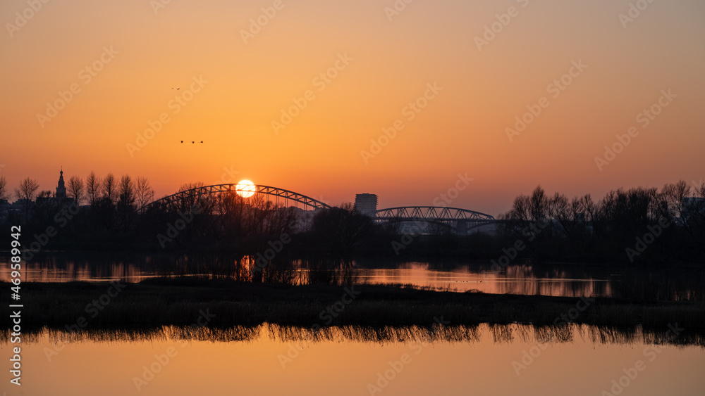 Setting sun behind the bridge over the Waal (Rhine) river in Nijmegen against an orange evening sky