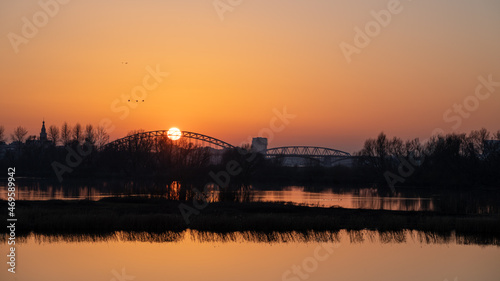Setting sun behind the bridge over the Waal (Rhine) river in Nijmegen against an orange evening sky