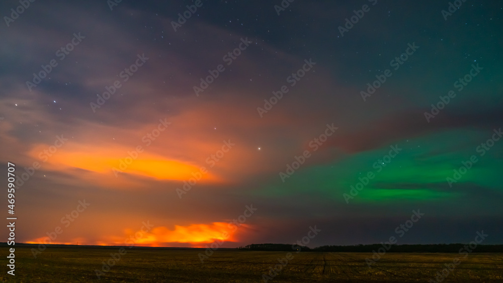 Obraz premium Northern lights battling the lights from a forest fire 