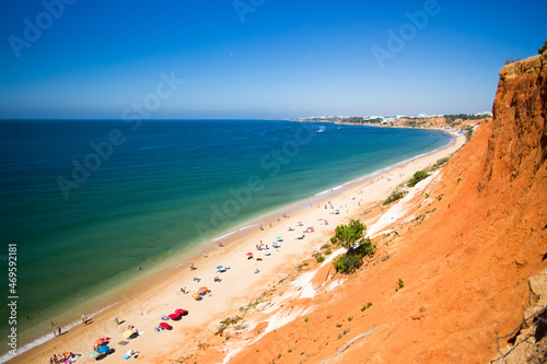 Orange cliff ending in the blue sea with tourists enjoying sun in "Falesia" in Algarve, Portugal