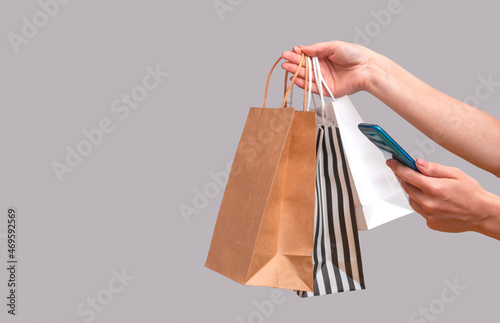 Woman shopping online from a mobile phone. Female hands with packages isolated on gray background, copy space