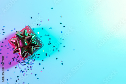 Neon Christmas winter background. Xmas gift box with shine lights. Holiday decoration on neon abstract gradient backdrop. Happy new year copy space.