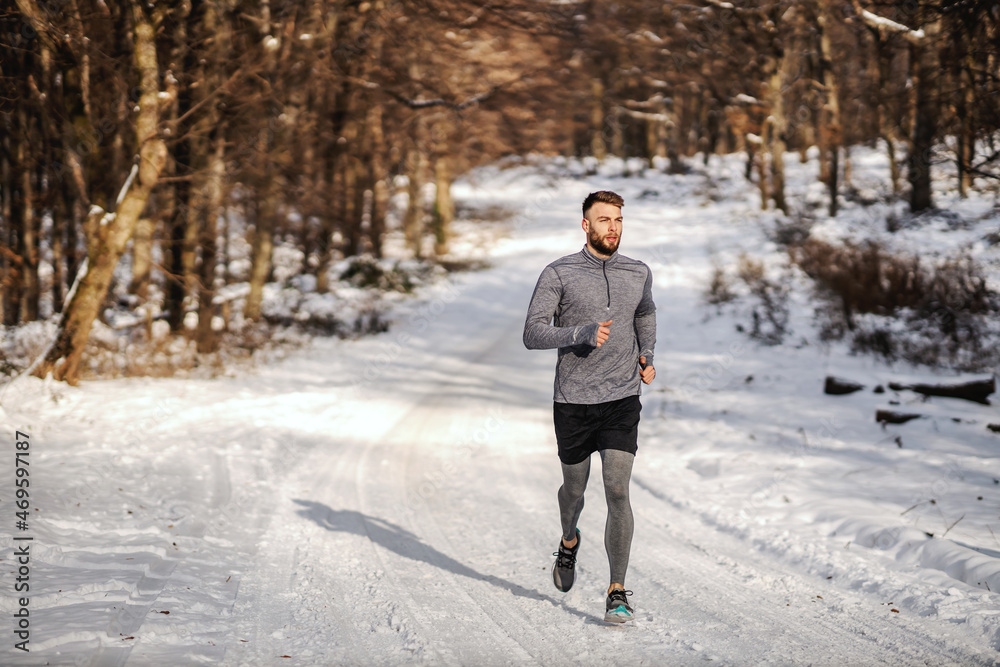 Fit sportsman running in forest at sunny snowy winter day. Outdoor fitness, cardio exercises, winter fitness