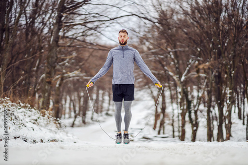 Fit sportsman jumping the rope in nature at snowy winter day. Winter fitness, cardio exercises