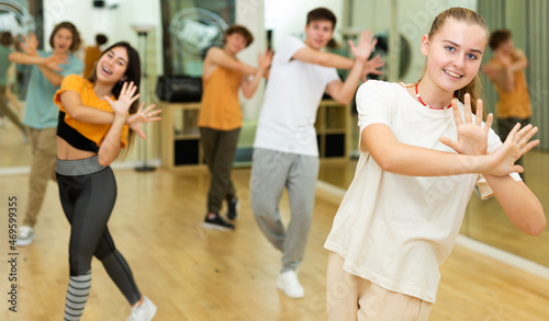 Portrait of cheerful teenage girl practicing energetic dance movements with group of teens in choreography class .