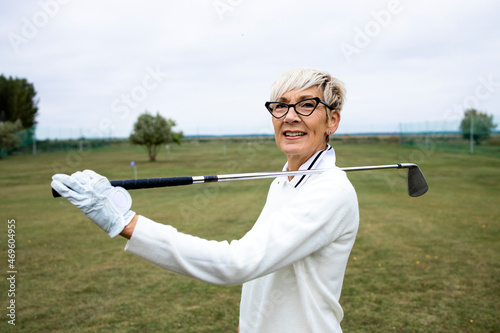 Portrait of female golfer with golf club standing on golf course.