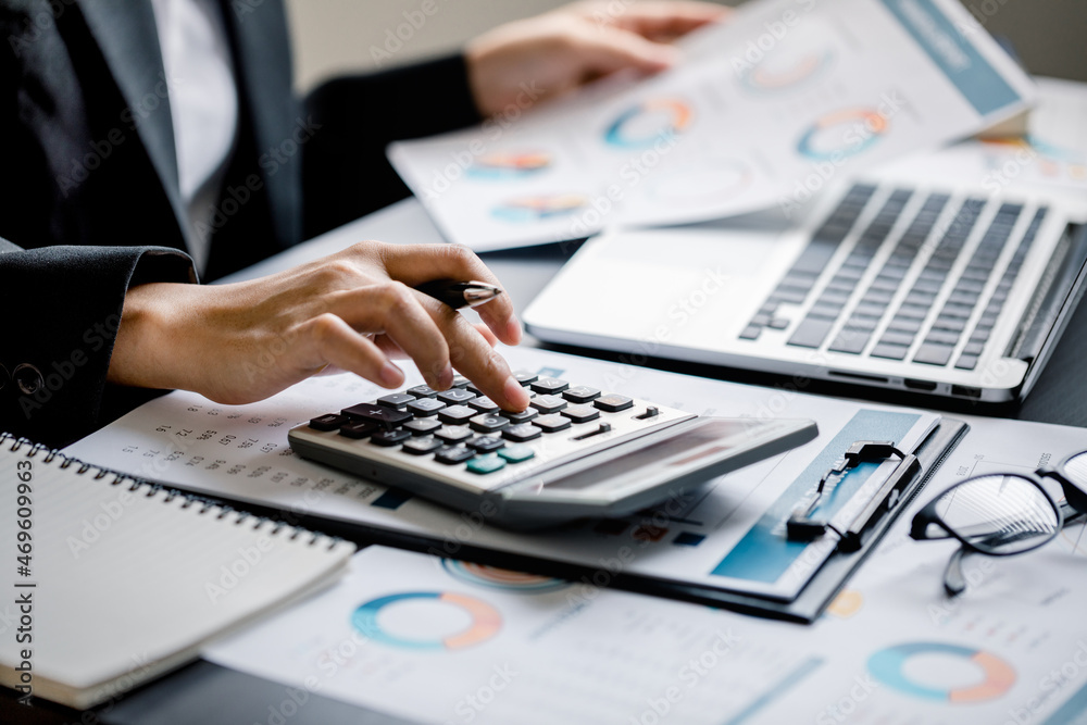 Close up of Businesswomen or Accountant using a calculator and laptop computer with analytic business report graph and finance chart at the workplace, financial and investment concept. Close up of Businesswomen or Accountant using a calculator and laptop computer with analytic business report graph and finance chart at the workplace, financial and investment concept.
