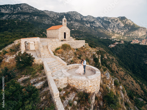The bride and groom are embracing on the observation deck near an ancient monastery in the mountains