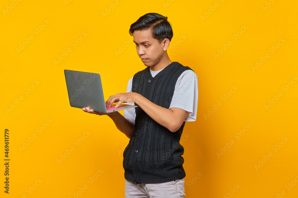 Portrait of handsome young man using laptop looking serious doing office work on yellow background Portrait of handsome young man using laptop looking serious doing office work on yellow background