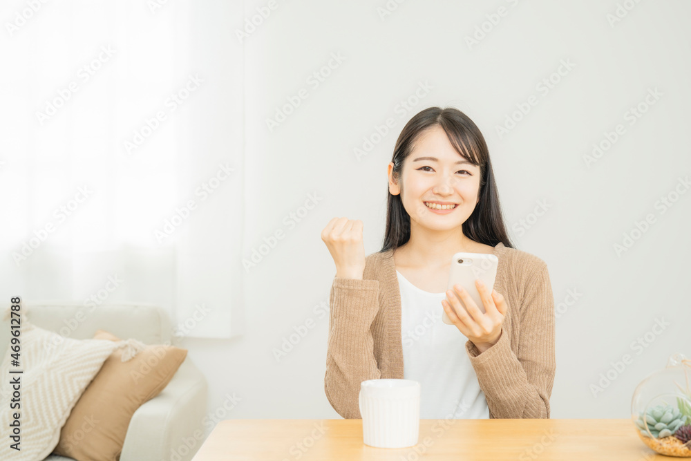 家でスマホを使う女性(ガッツポーズ)
家でスマホを使う女性(ガッツポーズ)